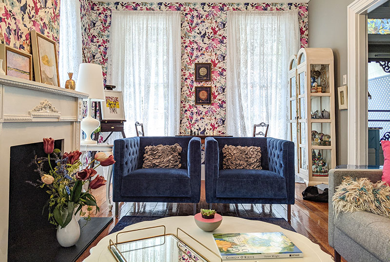 Twin blue velvet chairs in a gray living room with pink floral wallpaper