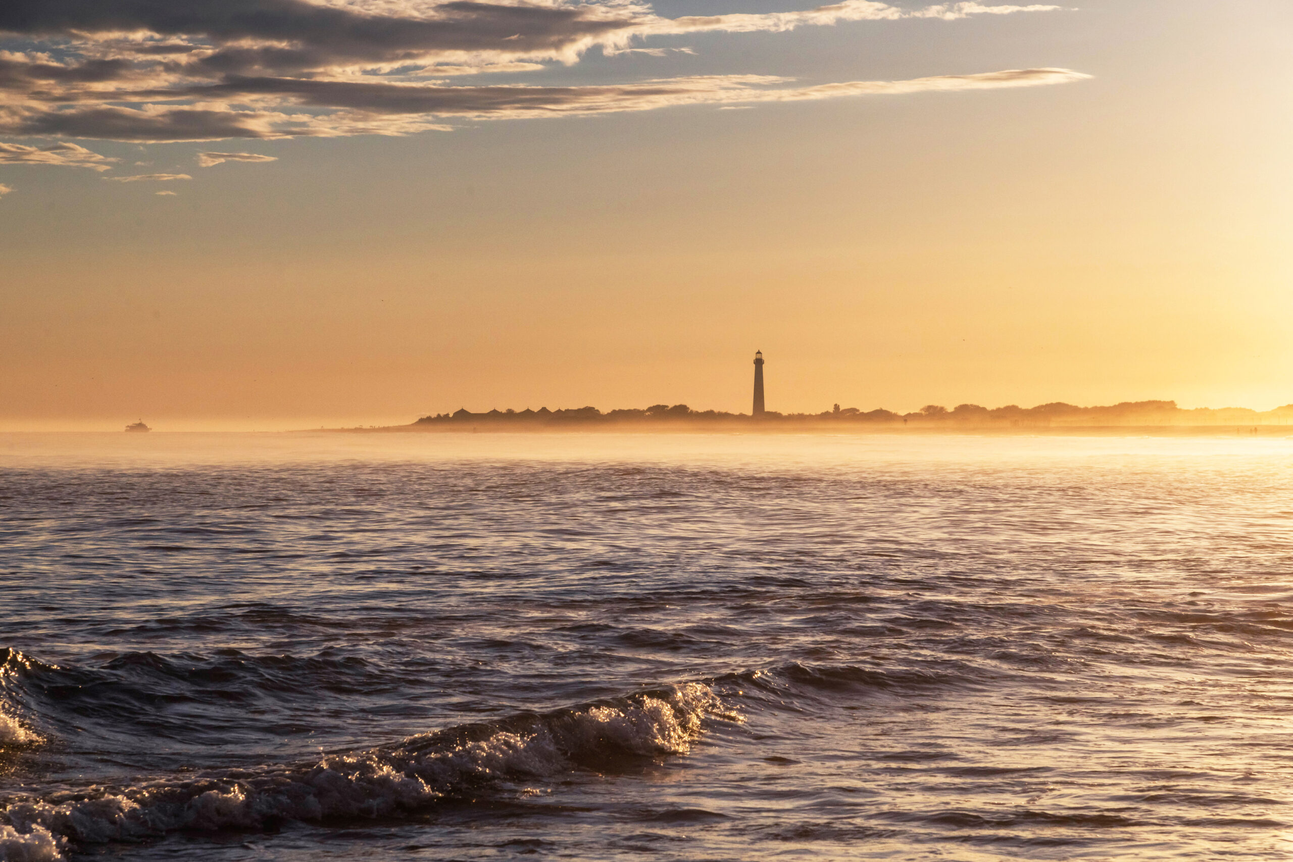 Misty golden light on the ocean in front of the Cape May Lighthouse at sunset.