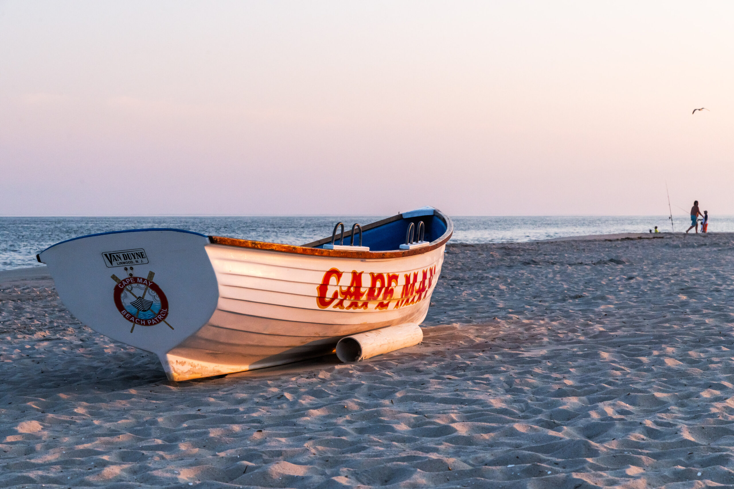 A Cape May lifeguard boat on the beach at sunset. There is pink light shining on the boat, and the sky is clear.