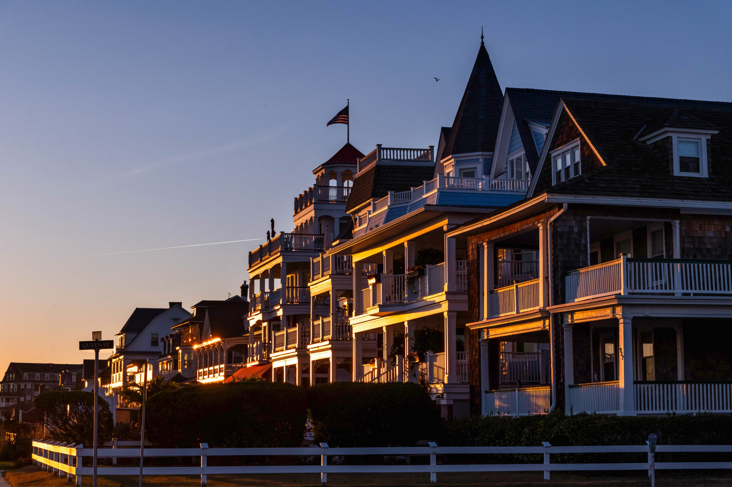 Victorian houses along Beach Ave in shadow with sunlight from the setting sun highlighting them. There is a clear blue and orange sky.