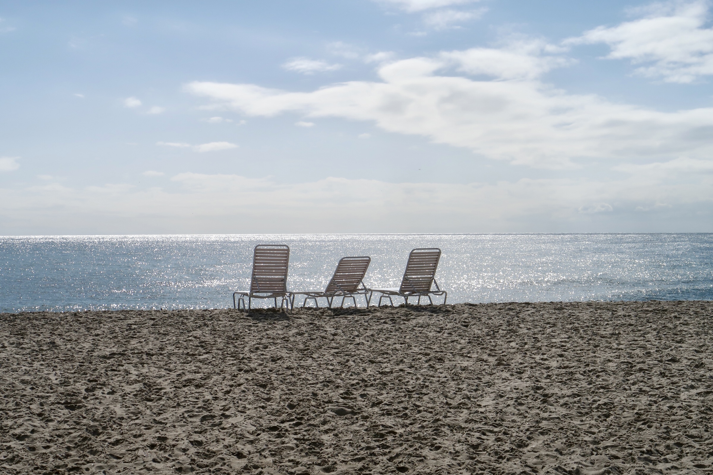 Three empty chairs on the beach facing the ocean