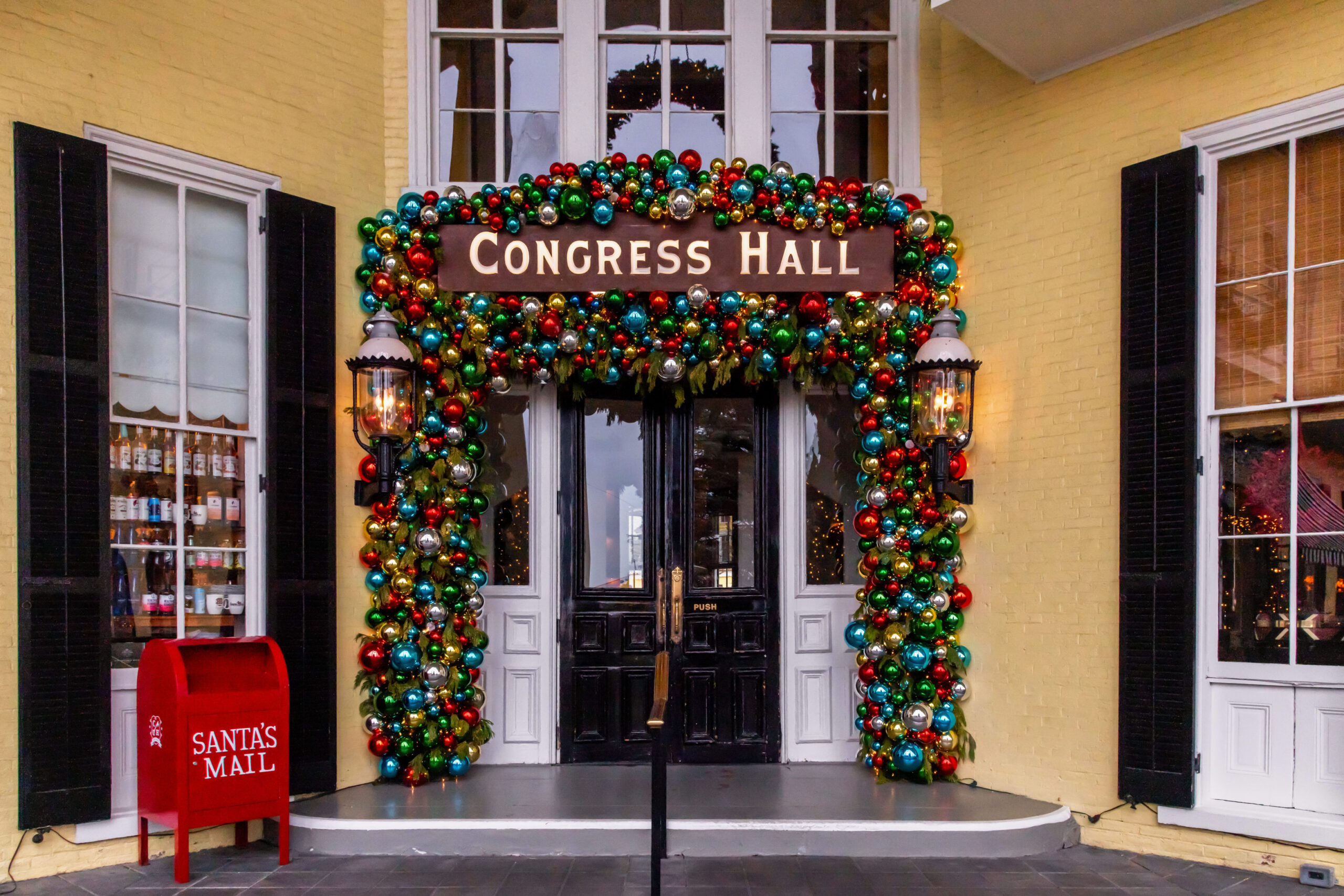 Colorful Christmas bulbs decorated around the Congress Hall sign and door. There are two lanterns next to the door, and a red Santa's Mail mailbox is to the left of the door.