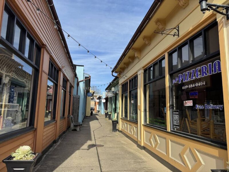 A view down Liberty Way of the brightly colored shops with a bright blue sky above and a strand of Christmas Lights crisscrossing the alleyway. 