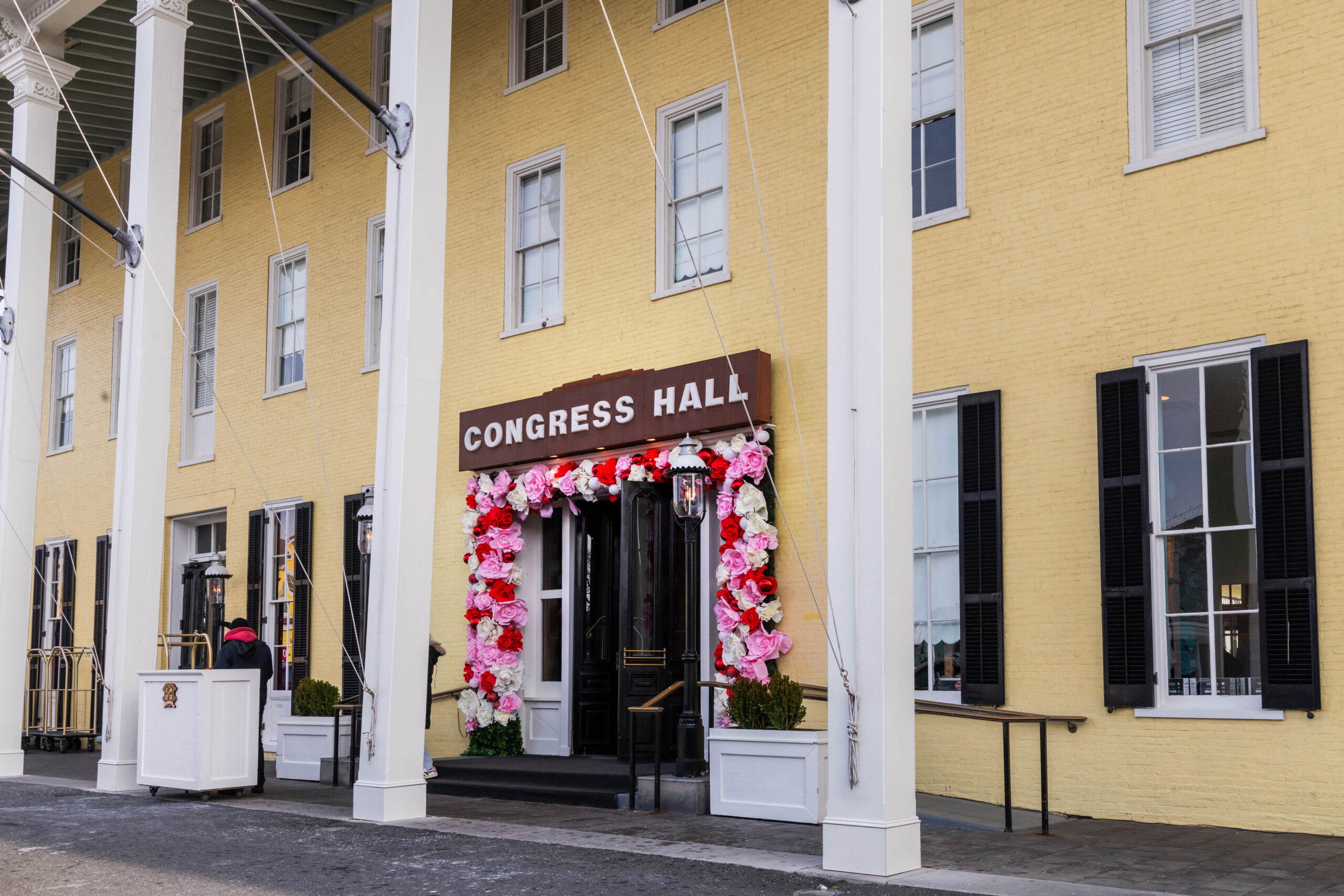 A wide view of the doorway of Congress Hall. There are pink and white roses around the door. There is a sign that says "CONGRESS HALL" above the door.