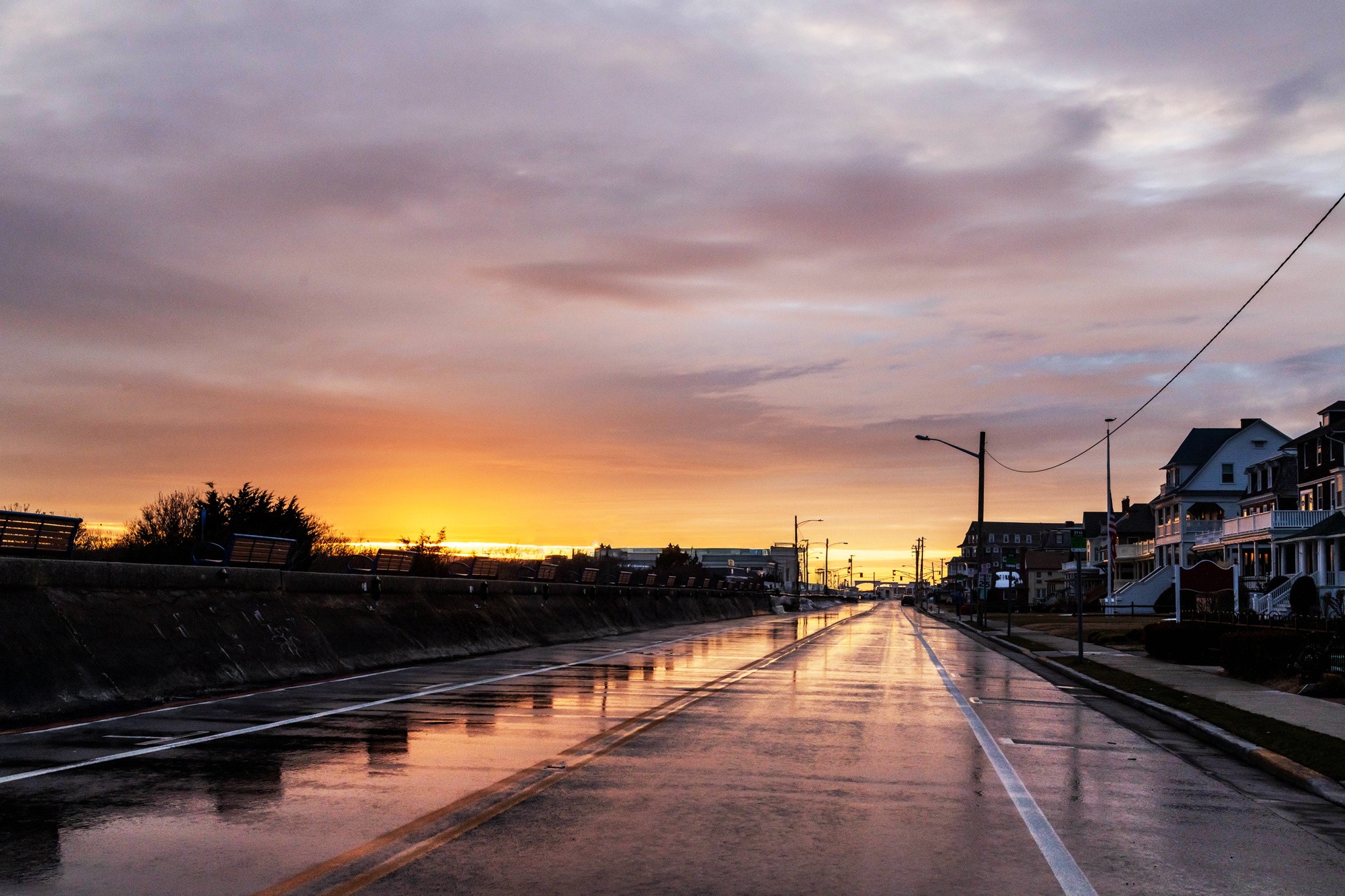 A wide view down Beach Ave after a storm. There are thin colorful clouds covering the sky, and the sun is shinning in the distance. The colors in the clouds are reflected on the wet street.