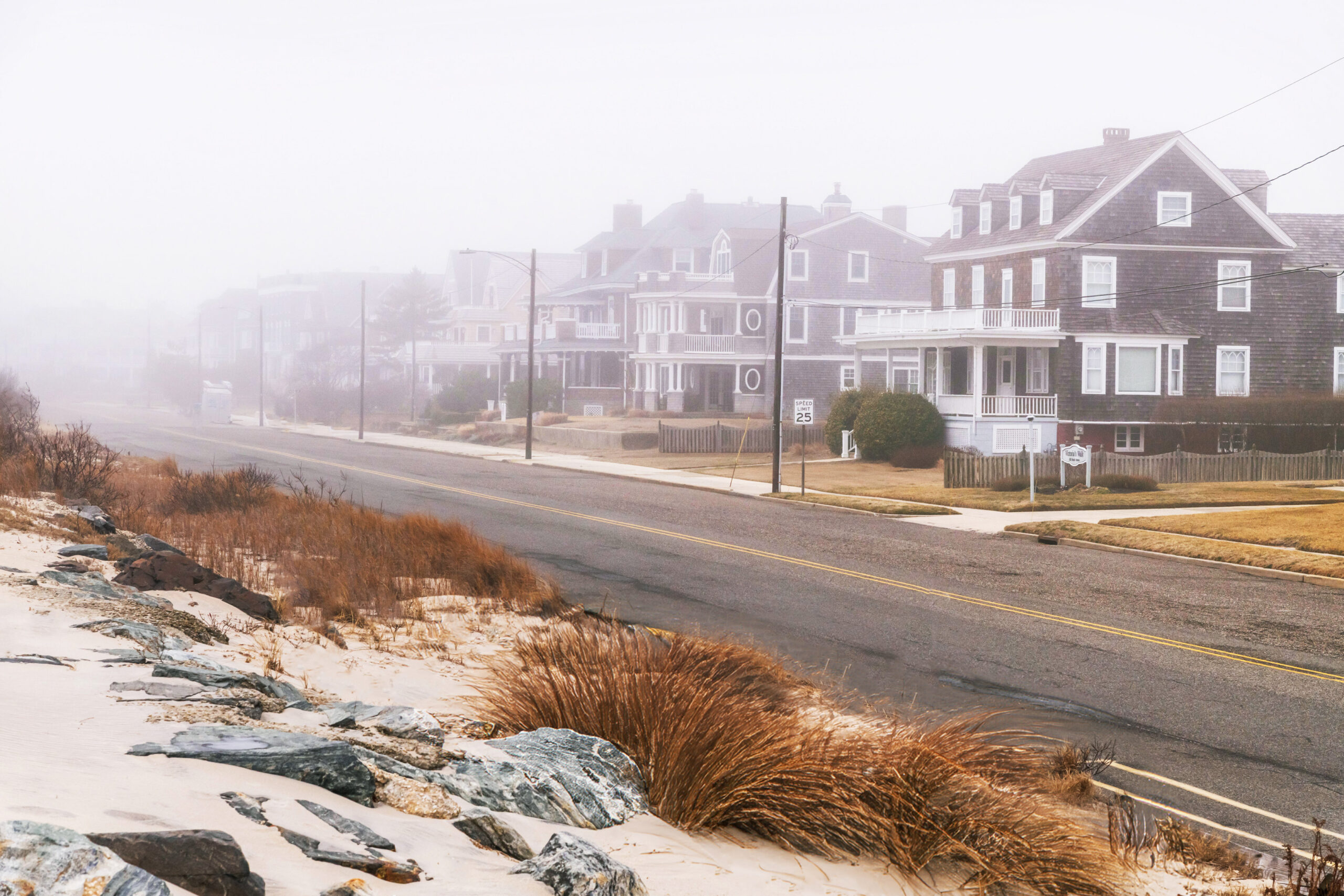 A wide view of the street of Beach Ave, beach houses, and beach dunes. Fog is obscuring the beach houses. 